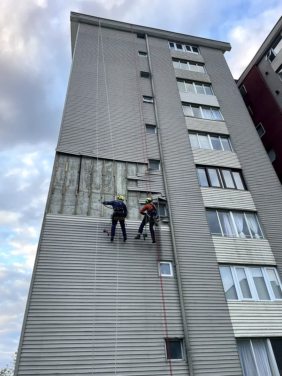 Técnicos de VERTEC reemplazando el revestimiento dañado de la fachada de un edificio con acceso por cuerdas