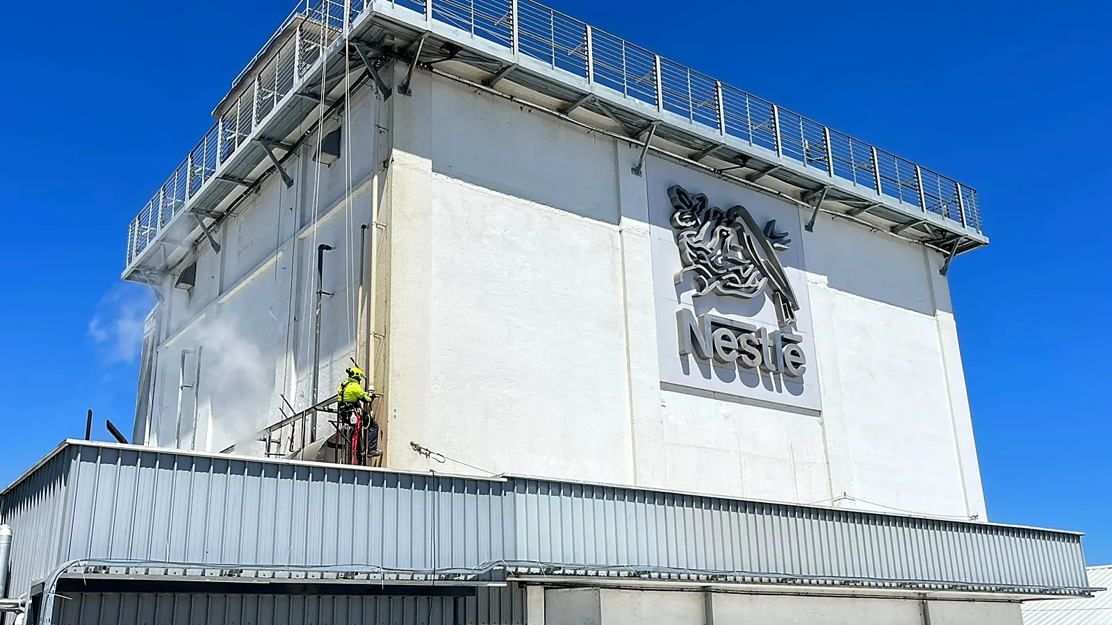 Técnico de VERTEC limpiando una bajada de aguas lluvia en la fachada de una planta industrial