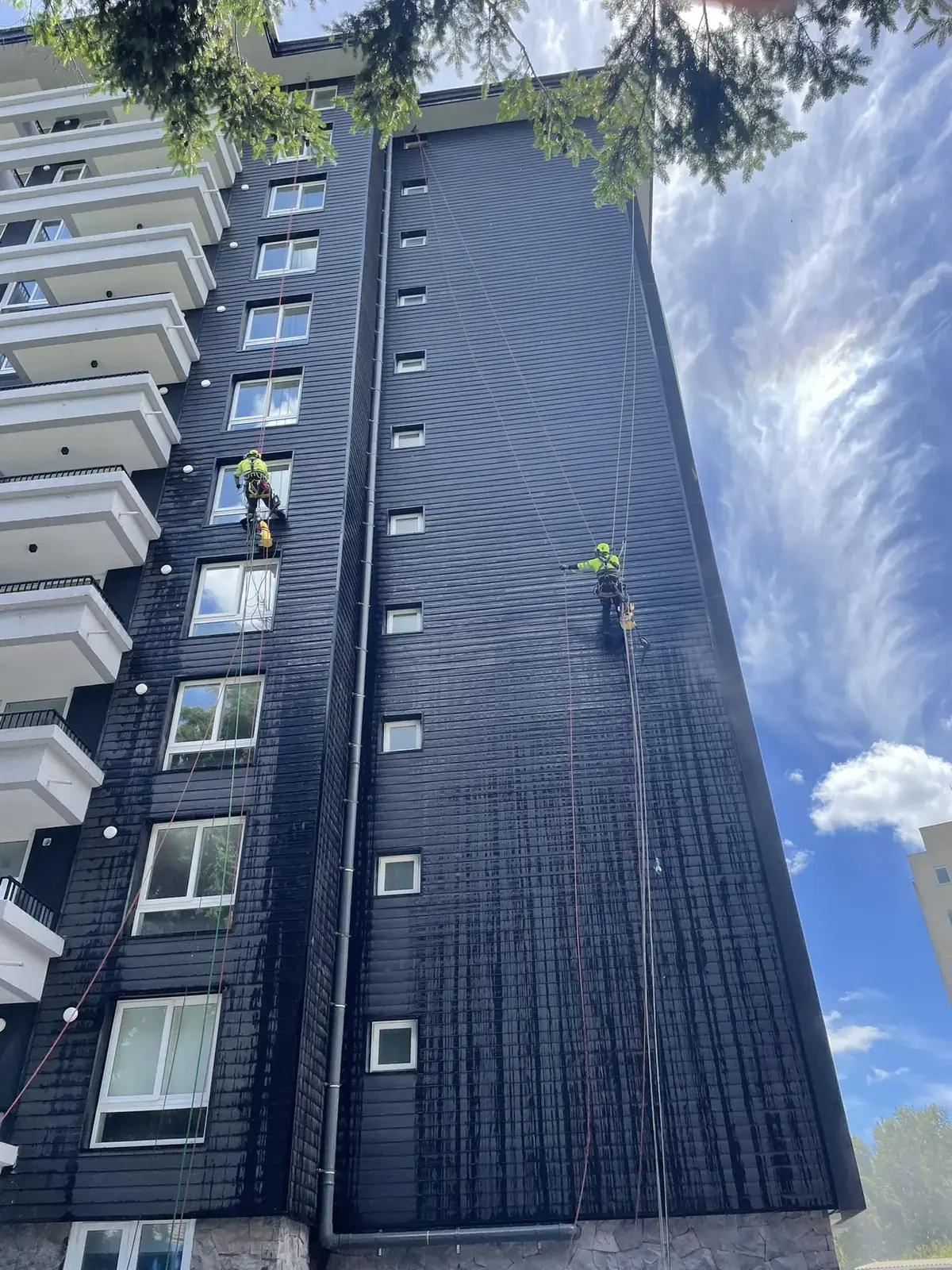 Técnicos de VERTEC limpiando la fachada de un edificio residencial de altura con acceso por cuerdas