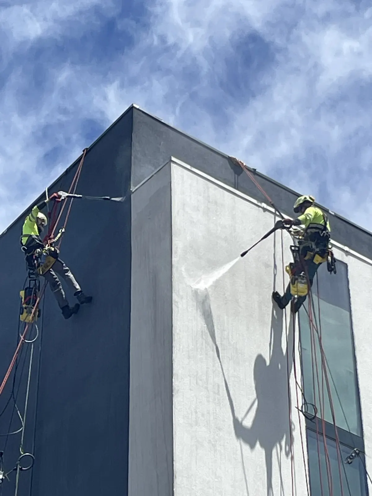 Dos técnicos de VERTEC limpiando con hidrolavado la esquina de un edificio con acceso por cuerdas