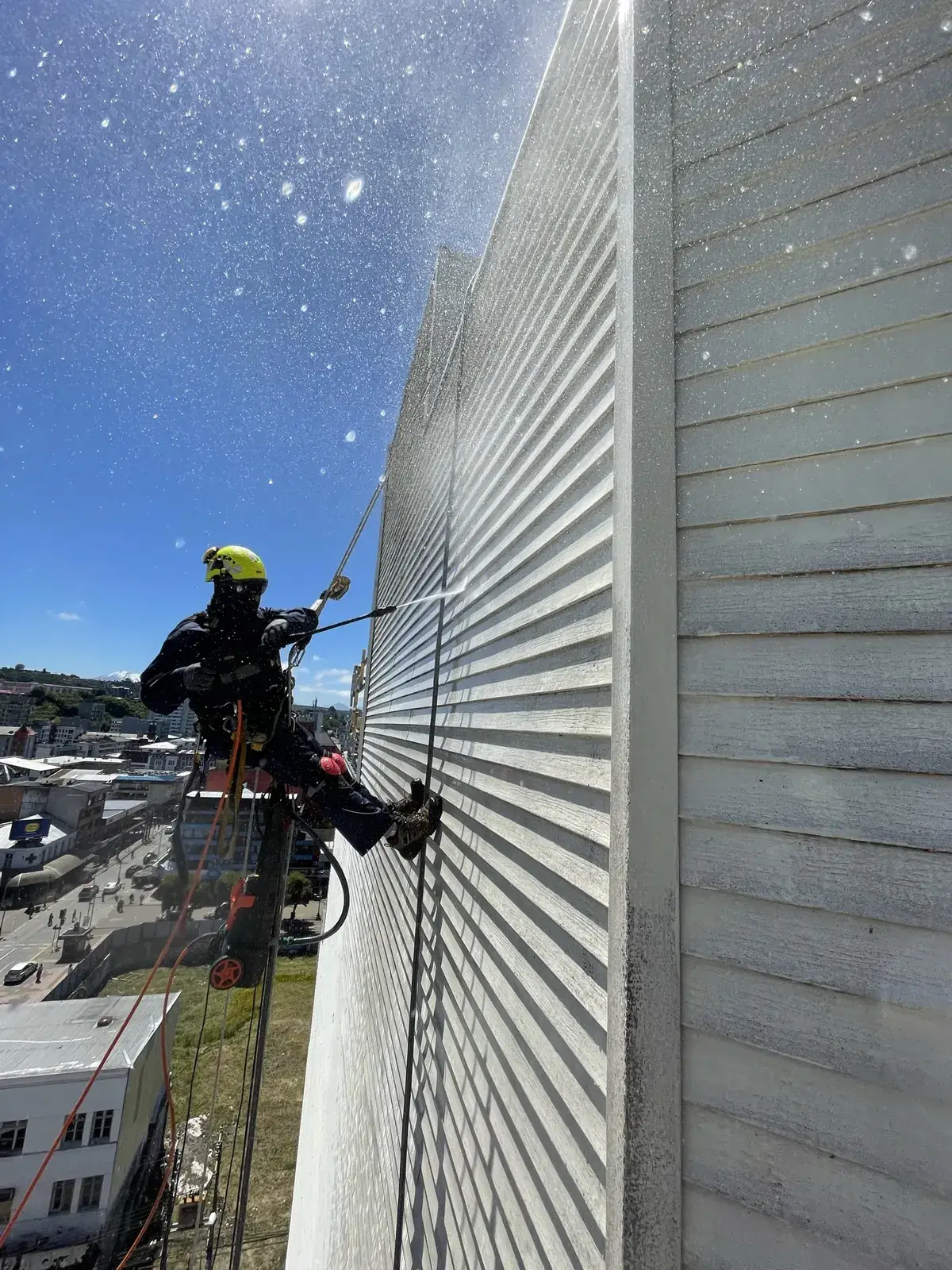 Técnico de VERTEC limpiando con hidrolavado la fachada de un edificio colgado con acceso por cuerdas