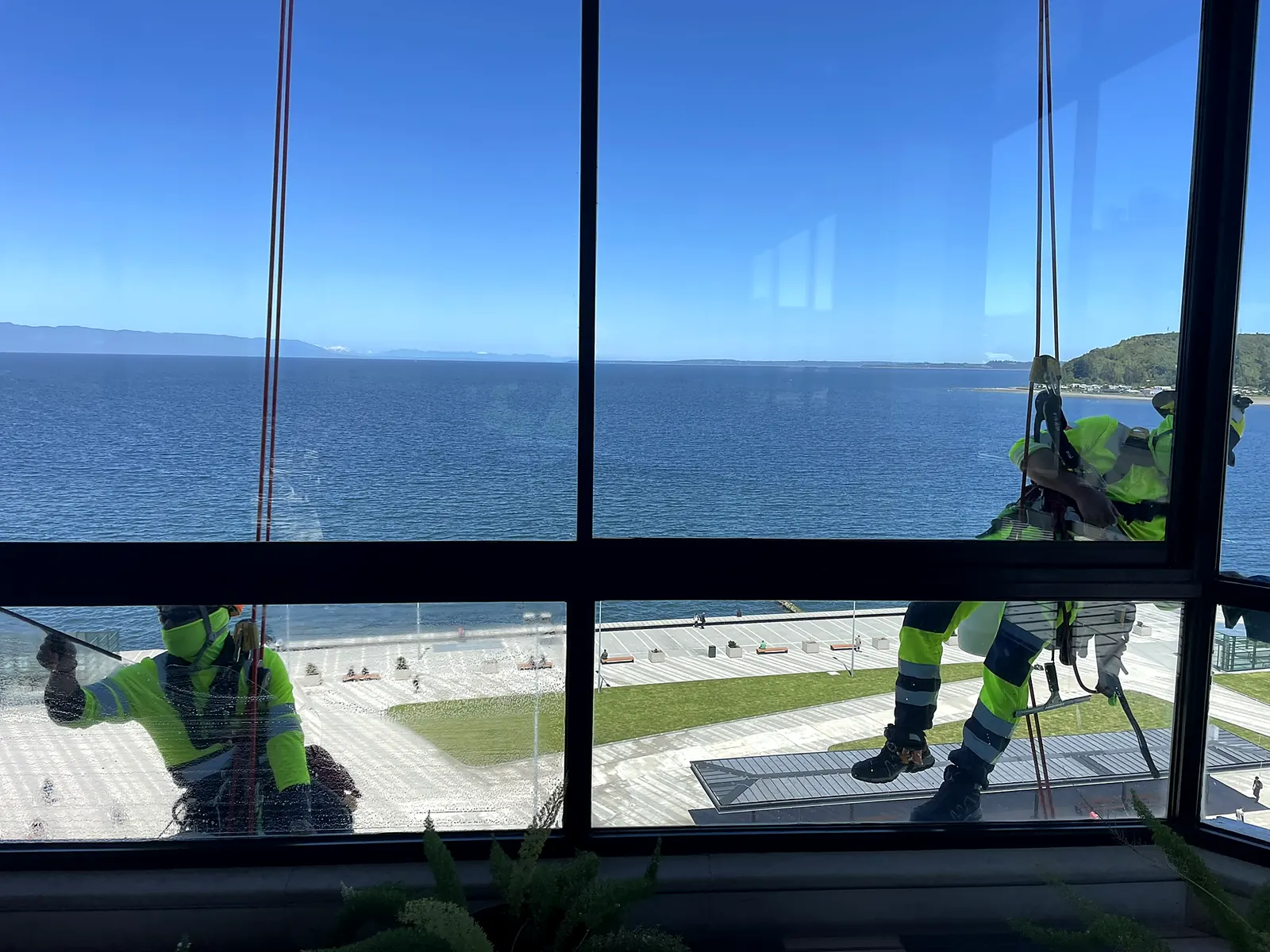 Técnicos de VERTEC limpiando por fuera los ventanales de un edificio frente al mar, vistos desde el interior