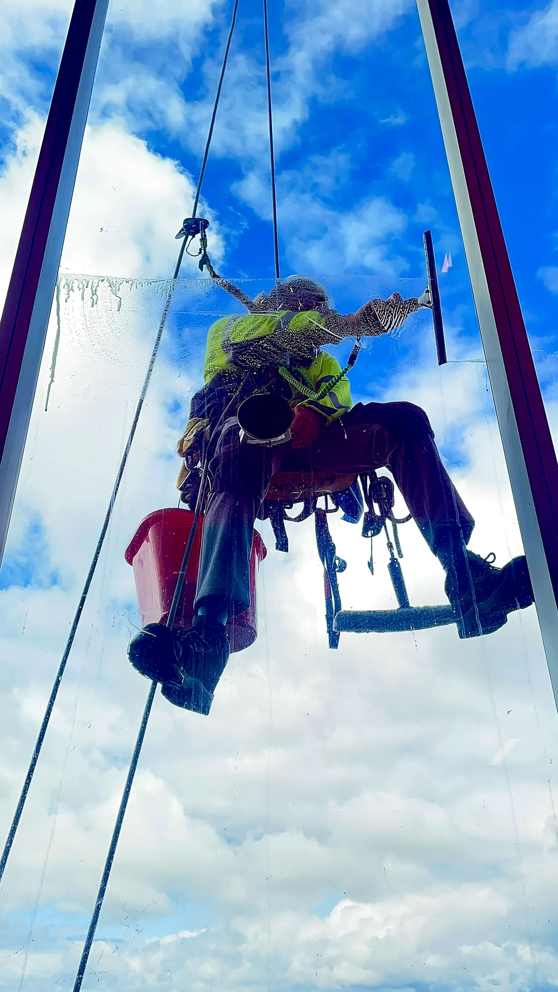 Técnico de VERTEC limpiando con rasqueta un ventanal en altura, visto desde el interior del edificio