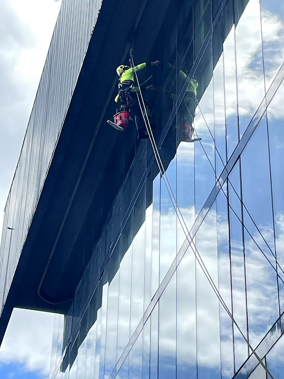 Técnico de VERTEC limpiando los vidrios bajo el voladizo de un edificio con acceso por cuerdas
