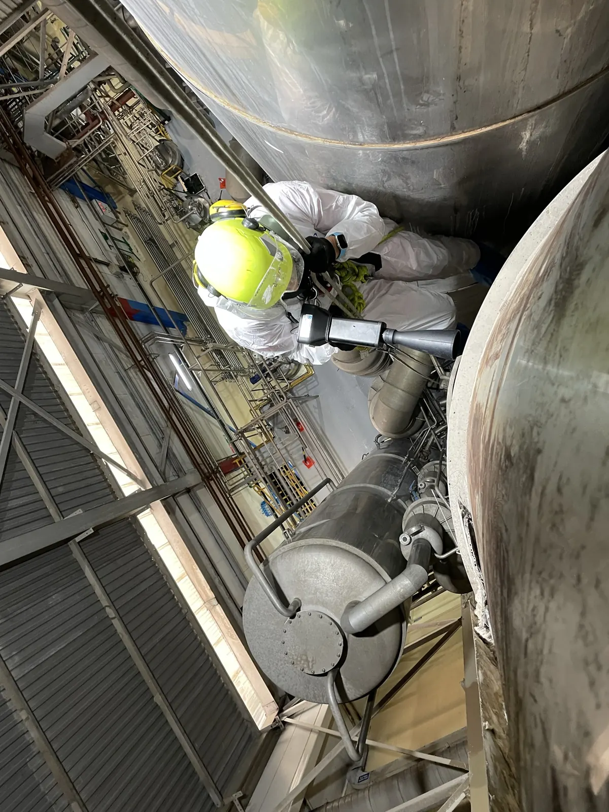 Técnico de VERTEC en acceso por cuerdas trabajando entre estanques y tuberías de una planta industrial